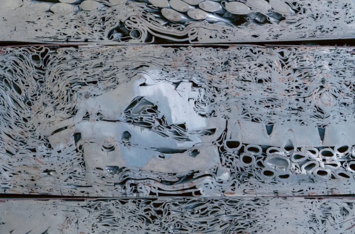Nahaufnahme dicht gepresster Metallteile mit gefalteten Blechstreifen und runden Öffnungen.